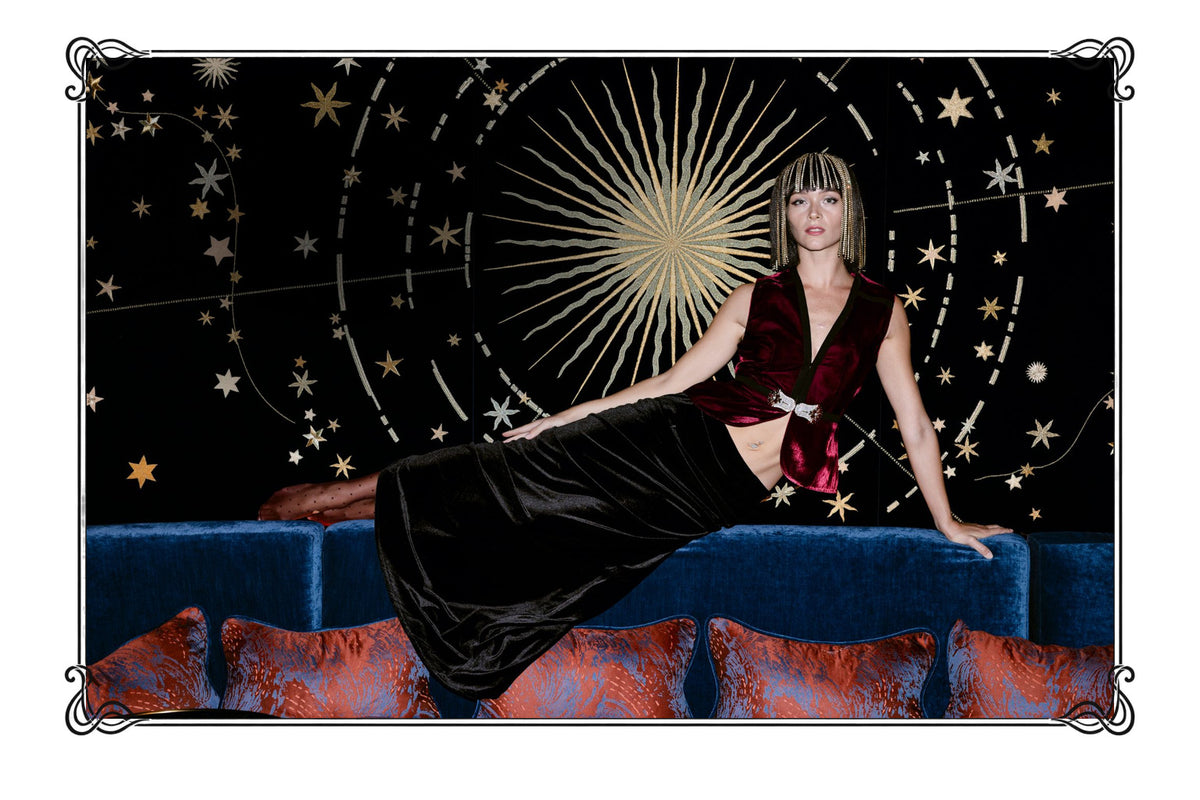Ludmilla campaign: the burgundy Nina velvet vest and Darya skirt in front of an embroidered star wall, in a black Art Nouveau frame