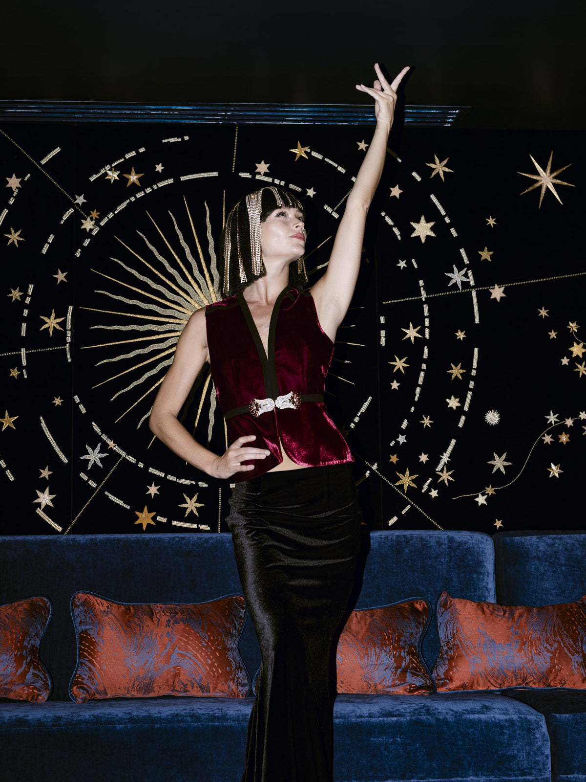 Model in the Nina burgundy velvet vest and the Darya velvet skirt before a celestial mural — Ludmilla collection